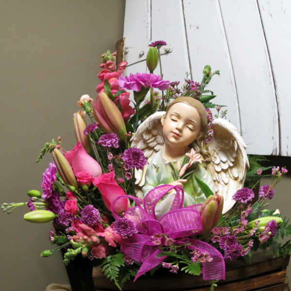 Pink and purple floral arrangement with an angel figurine and ribbon