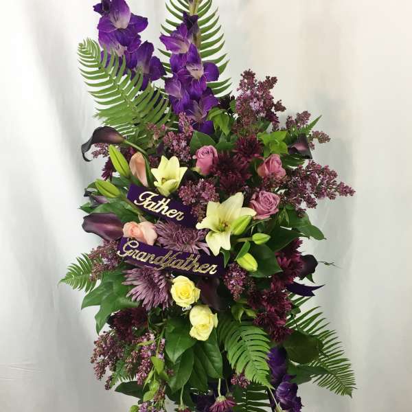 Tall funeral spray with purple flowers and ribbons reading Father and Grandfather