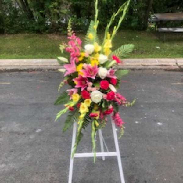 Tall standing floral spray with pink, yellow, and white flowers on a white easel