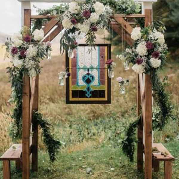 Floral-decorated wooden wedding arch with hanging glass jars