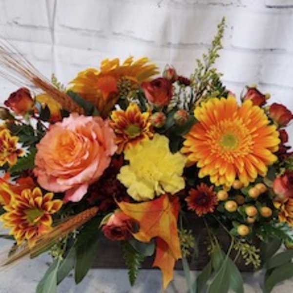 Autumn floral arrangement with orange and yellow blooms in a low container