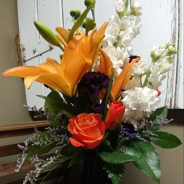 Orange lilies and white flowers in a tall vase
