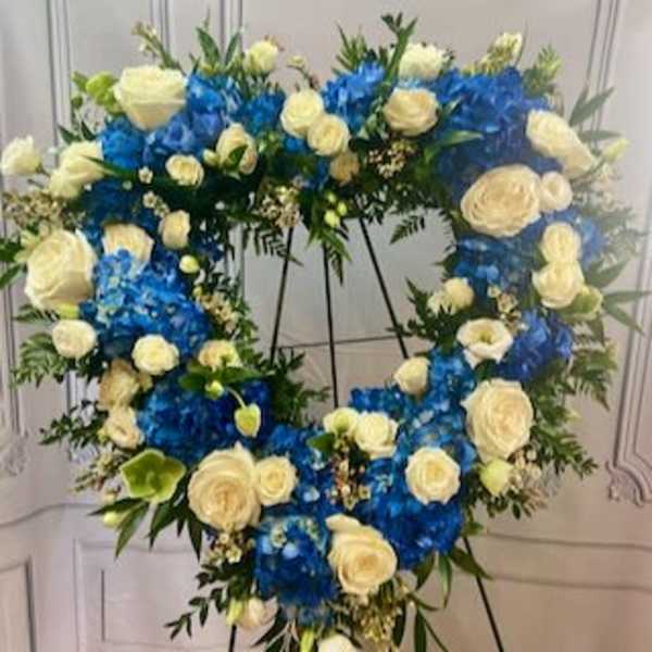 Heart-shaped floral wreath with blue and white roses on a stand