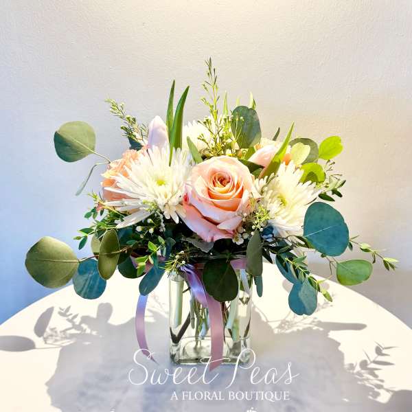Peach roses and white flowers in a clear glass vase with eucalyptus