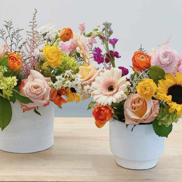 Two colorful flower arrangements in white pots on a table