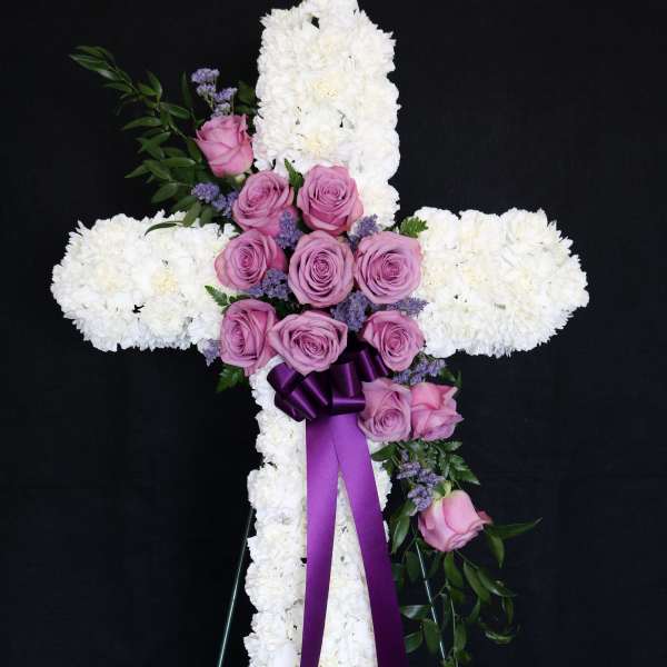 White floral cross with pink roses and a purple ribbon on an easel