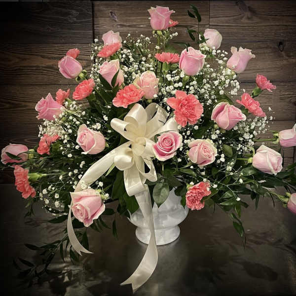 Pink roses and carnations in a white vase with a cream ribbon