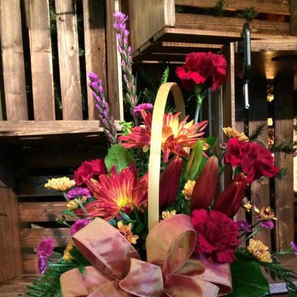 Basket arrangement of red, pink, and yellow flowers with a large ribbon bow