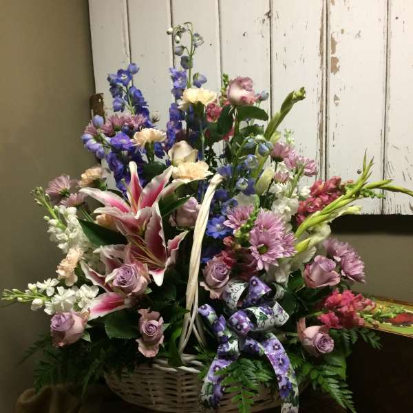 Basket arrangement with pink lilies, lavender roses, and blue flowers