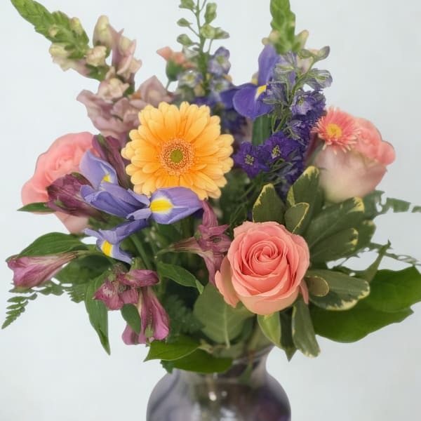 Mixed bouquet of pink, purple, and yellow flowers in a glass vase