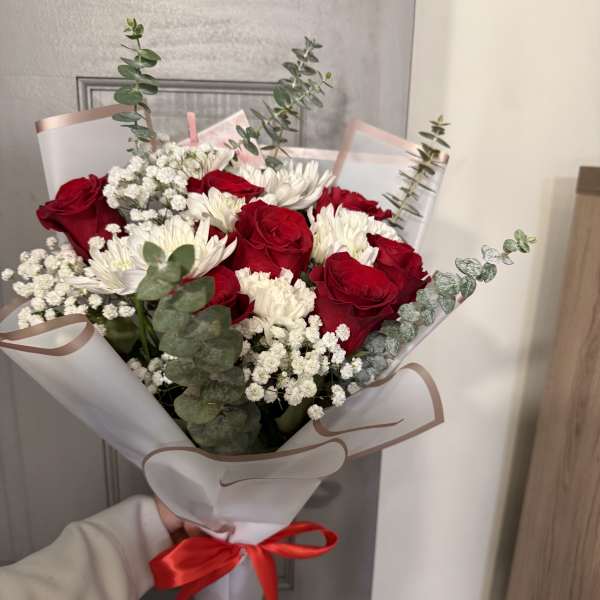 Bouquet of red roses and white daisies wrapped in white paper with a red ribbon
