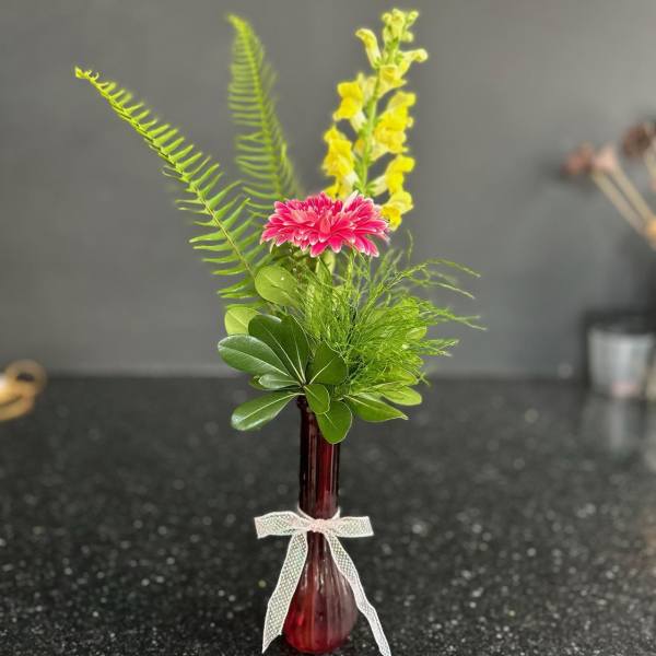 Small pink and yellow floral arrangement in a red glass vase
