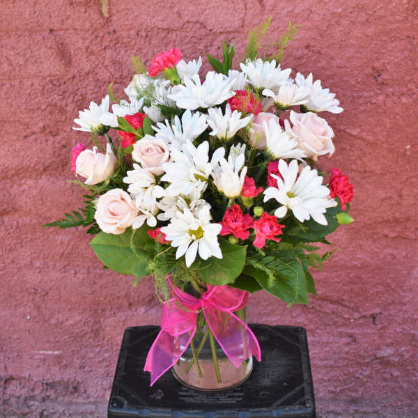 Bouquet of white daisies and pink roses in a glass vase with a pink ribbon