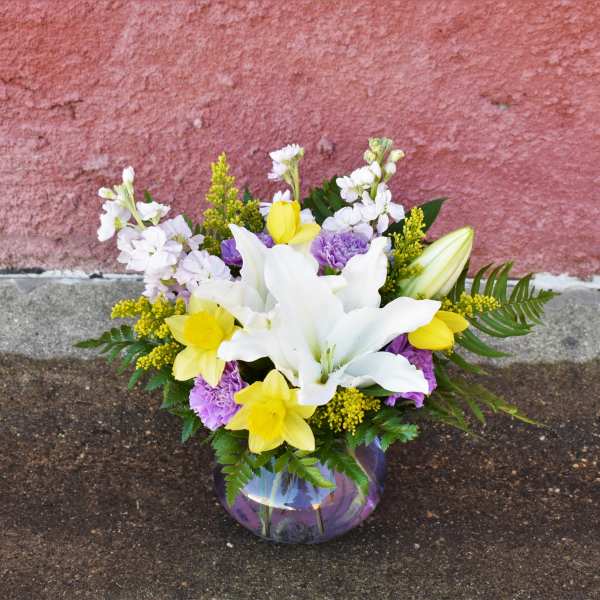 Bouquet of white lilies, yellow daffodils, and purple carnations in a glass vase
