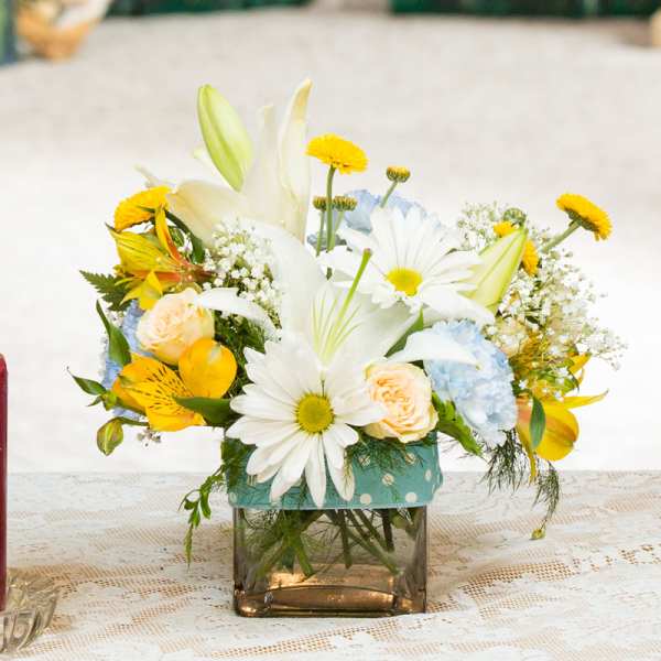 Mixed bouquet of white lilies, daisies, and pastel roses in a square glass vase