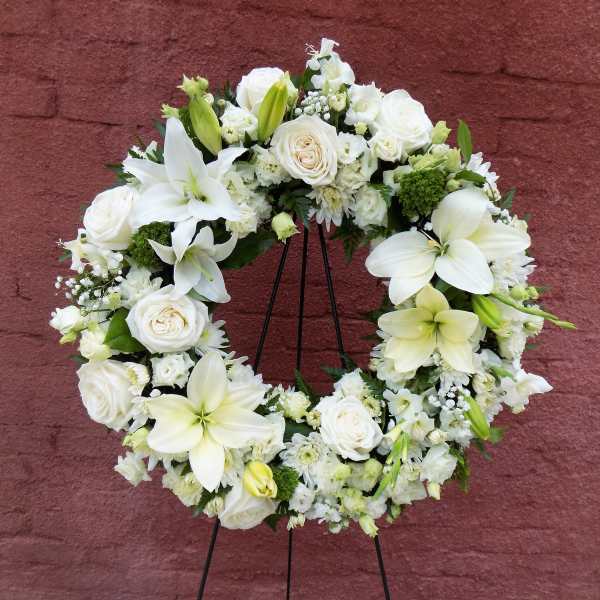 White floral wreath on a black stand with roses and lilies