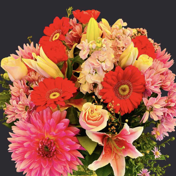 Bright mixed bouquet in a green vase with pink, red, and yellow blooms