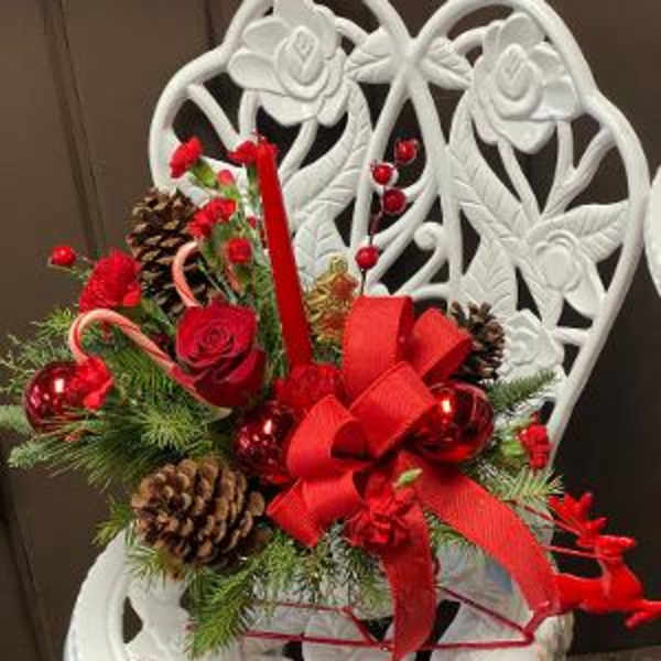 Holiday arrangement with red roses, pinecones, candy canes, and a red bow in a white chair