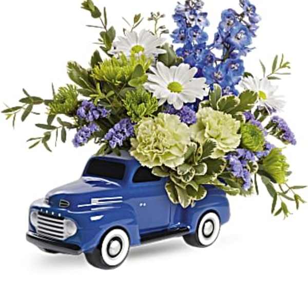 Blue truck-shaped planter filled with white, blue, and green flowers