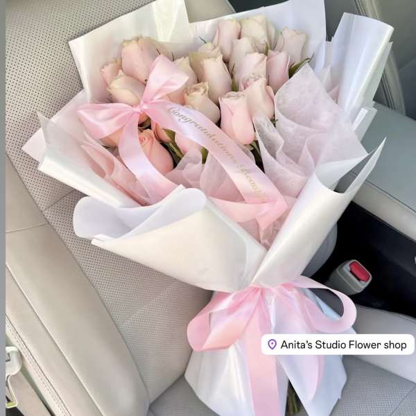 Bouquet of pale pink roses wrapped in white and pink paper with a ribbon