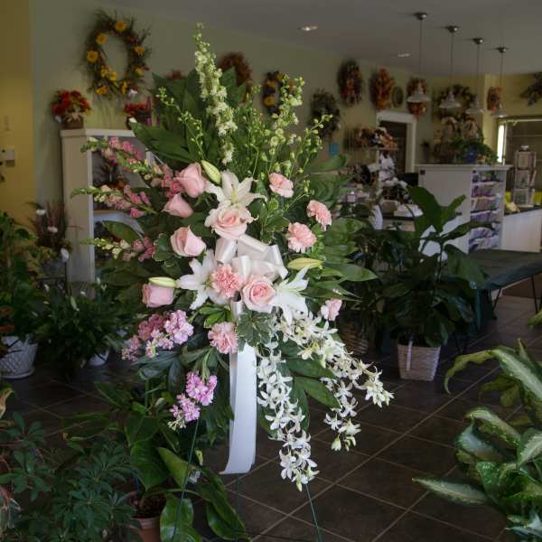Tall floral standing spray with pink roses, white lilies, and cascading white orchids