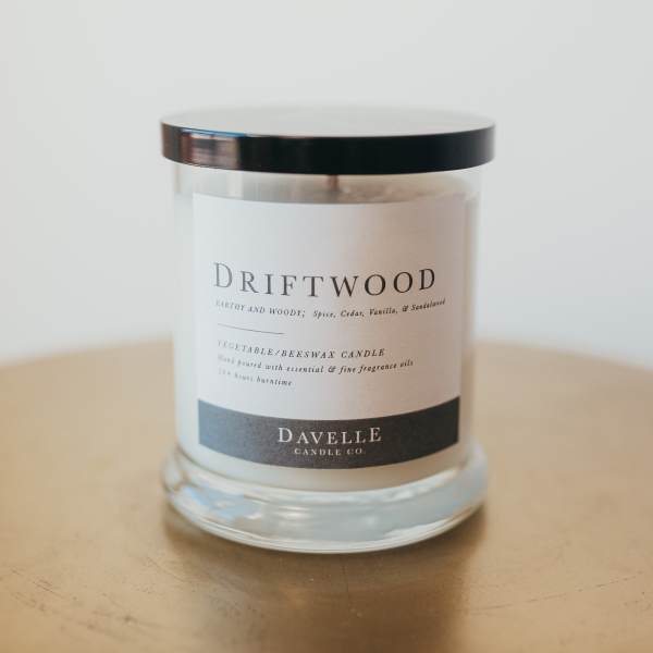 A driftwood-scented candle in a clear glass jar with a black lid