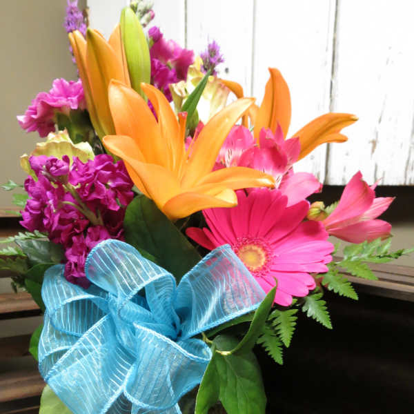 Bright mixed bouquet with orange lilies, pink gerbera daisies, and a blue ribbon