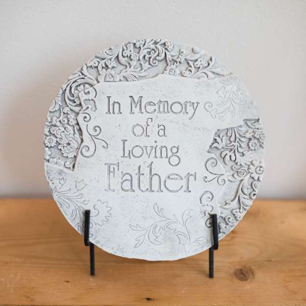 Round memorial plaque reading "In Memory of a Loving Father" on a stand