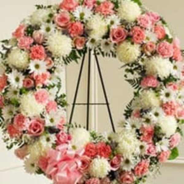 Pink and white floral wreath on a black stand