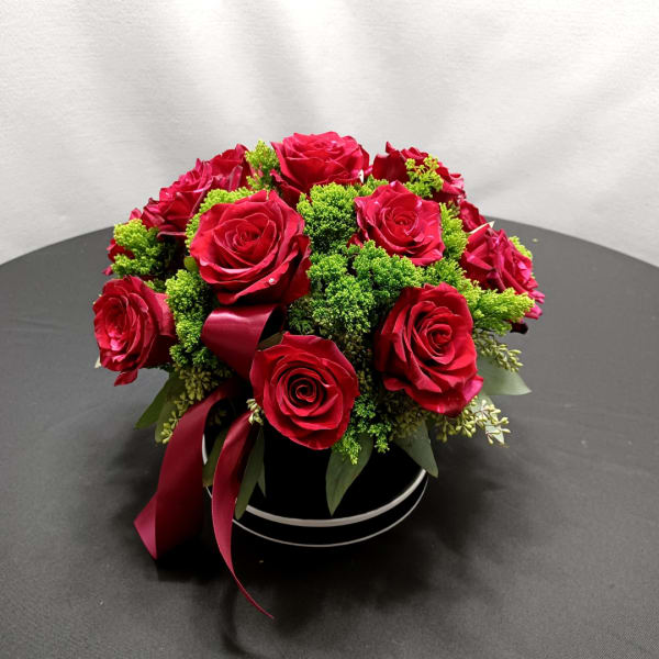 Red roses arranged in a black round box with burgundy ribbon