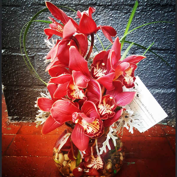 Red orchids arranged in a round glass vase with decorative stones