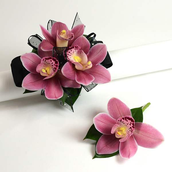 Pink cymbidium orchid wrist corsage with black ribbon and matching boutonniere on white surface