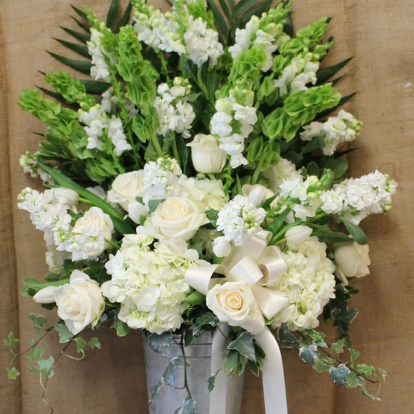 White roses and hydrangeas in a tall silver vase with a ribbon