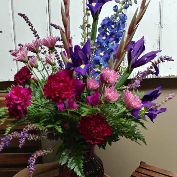Tall mixed bouquet of purple, pink, and blue flowers in a dark glass vase