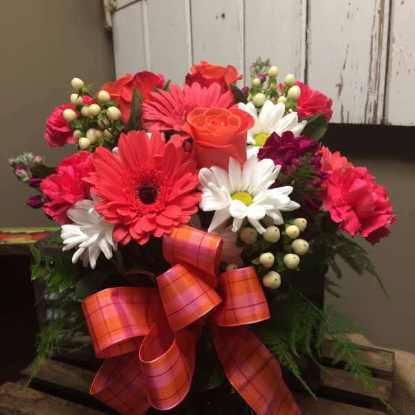 Bouquet of pink and orange flowers with a plaid ribbon in a dark container
