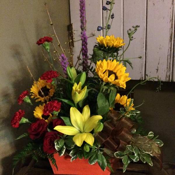 Mixed bouquet with sunflowers, lilies, roses, and carnations in a red container