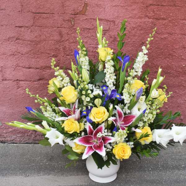 Mixed bouquet of yellow roses, white lilies, and blue irises in a white vase