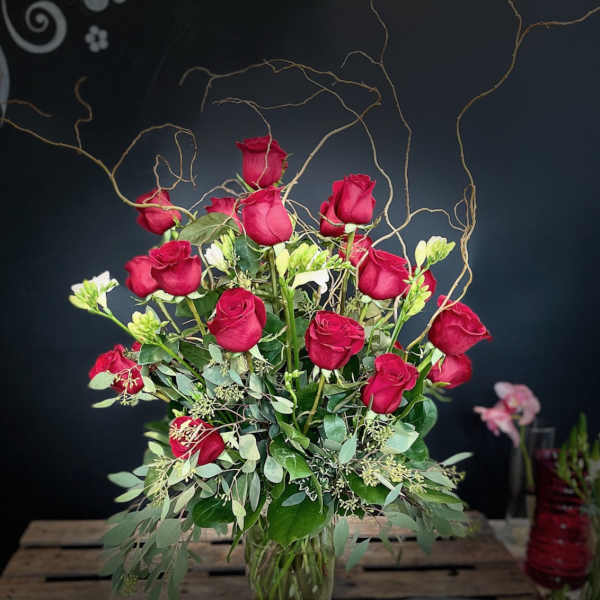 Tall bouquet of red roses in a glass vase with curly branches