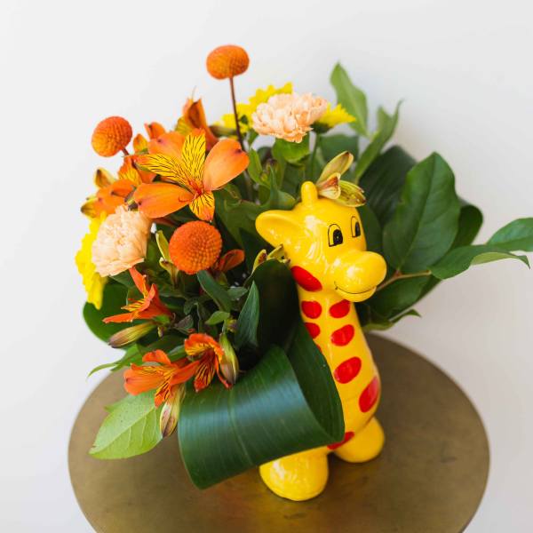 Orange and yellow flower arrangement in a yellow giraffe vase