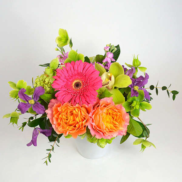 Bright mixed bouquet in a white vase with pink, orange, purple, and green blooms