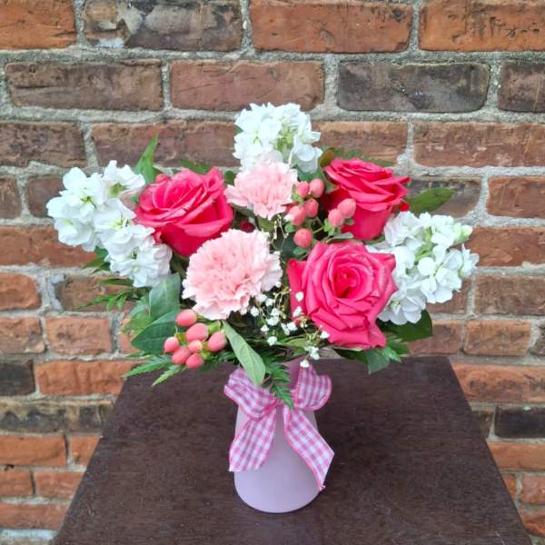 Pink roses and carnations in a vase with white flowers and a gingham ribbon