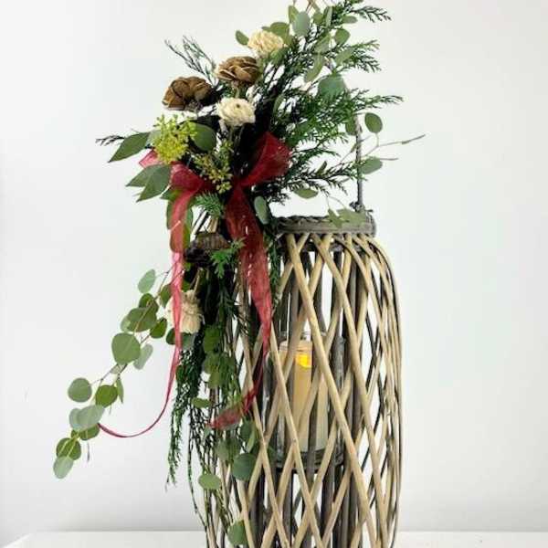 Tall floral arrangement in a woven lantern-style vase with red ribbon