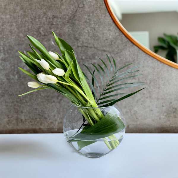 White tulips in a round glass vase with palm leaves
