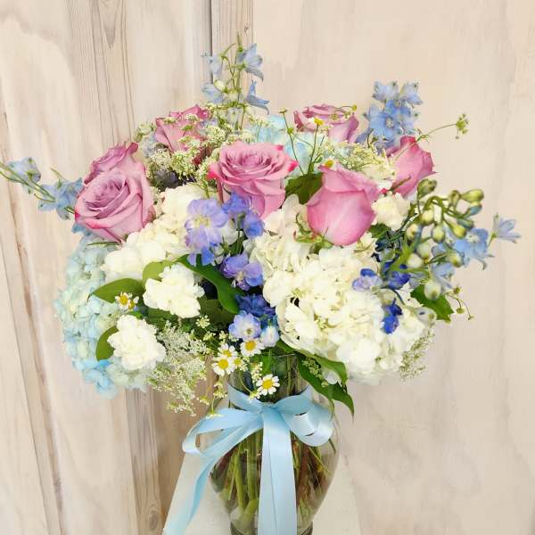 Pink roses and blue flowers in a glass vase with a blue ribbon