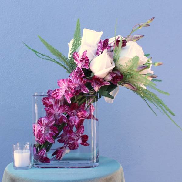 Pink and white orchid arrangement in a clear glass vase with fern accents