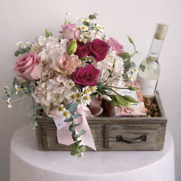 Pink and white flower bouquet in a wooden box with a bottle of wine
