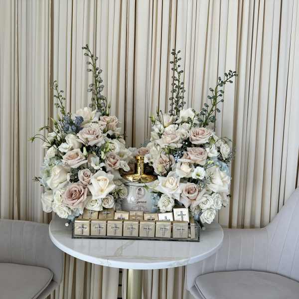 Two pastel floral arrangements flank a gold bottle on a table