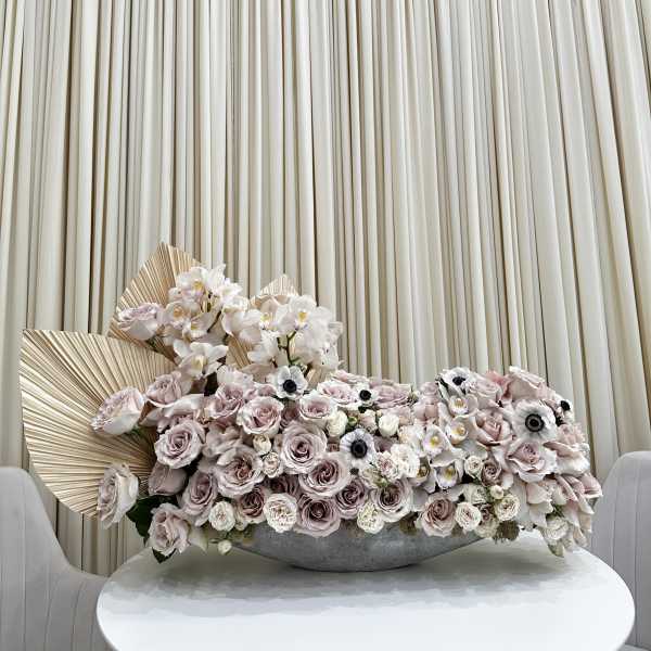 Large pastel floral arrangement with roses and orchids in a low gray bowl