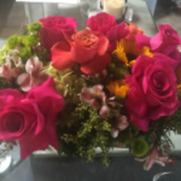 Compact arrangement of hot pink and orange roses with yellow blooms in a glass vase