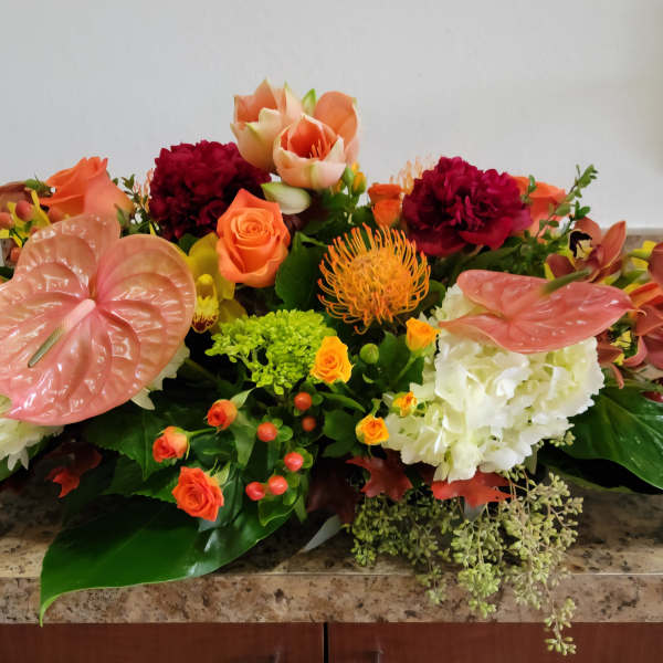 Low floral arrangement with pink anthuriums, orange roses, and white hydrangeas